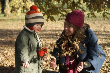 Mother and son playing with autumn leaves in the park