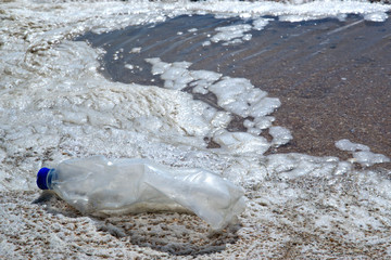 CSR Corporate Social Responsibility ecology concept. Plastic bottle on a dirty beach in dirty sea...