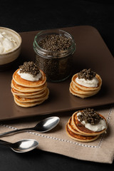 Black caviar, curd cheese, mini pancakes, blackberries on a wooden background.