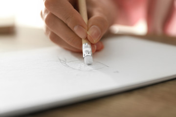 Woman correcting picture in notepad with pencil eraser at table, closeup