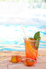 Delicious refreshing drink and sunglasses near swimming pool
