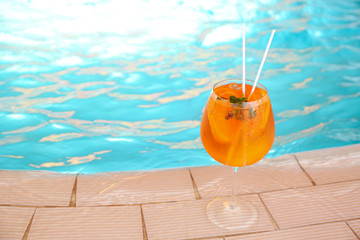 Glass of delicious cocktail near swimming pool, space for text. Refreshing drink
