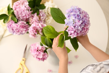 Woman making bouquet with beautiful hydrangea flowers indoors, closeup. Interior design element