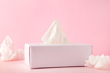 Box with paper tissues and used crumpled napkins on pink background