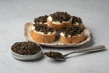 Black caviar in a jar and on a spoon. Sandwiches with black caviar on a plate. An exquisite delicacy.