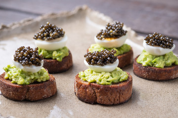 Sandwiches on Borodino bread with avocado paste, quail egg and black caviar