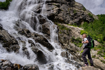 Obraz premium Man hiking with backpack looking at waterfall. Portrait of male adult back standing outdoor.