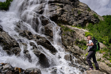 Man hiking with backpack looking at waterfall. Portrait of male adult back standing outdoor.