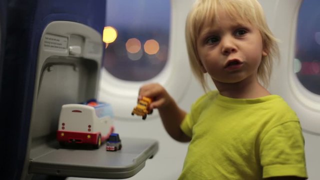 Toddler boy, child boarding on the airplane, sitting and waiting for departure, playing with toys, smiling happily