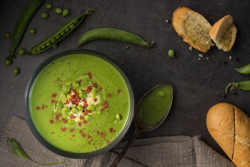 Healthy vegetarian creamy green peas soup with toasted garlic bread, spoon on the table in rustic style. Fresh pea pods from garden