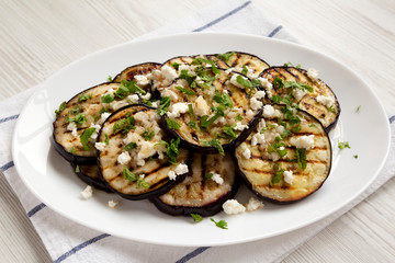 Homemade Grilled Eggplant with Feta and Herbs on a white plate, side view. Close-up.