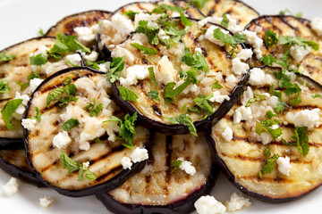 Homemade Grilled Eggplant with Feta and Herbs on a white plate, low angle view. Close-up.