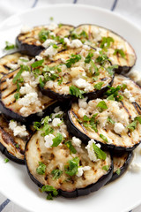 Homemade Grilled Eggplant with Feta and Herbs on a white plate on cloth, side view.