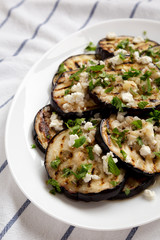 Homemade Grilled Eggplant with Feta and Herbs on a white plate on cloth, side view.