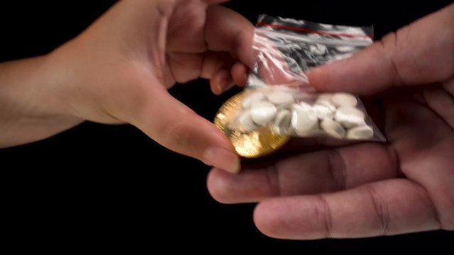 close up view of Bitcoin cryptocurrency being used to buy black market drugs, a small transparent bag with grey pills on black background 4k