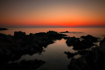 Fototapeta na wymiar Sonnenaufgang über dem Wasser mit Felsen und Spiegelung