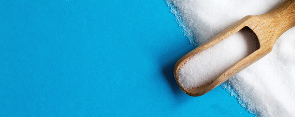 Fototapeta na wymiar Salt grain in wooden spoon top view on a blue background , flat lay. banner