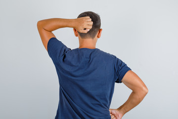 Young man scratching his head in dark blue t-shirt , back view.