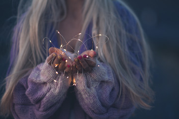 Woman holding sparkling lights in hands closeup. Celebration. Winter holiday season.