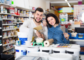 Young loving couple demonstrating tools for house renovating in paint supplies store