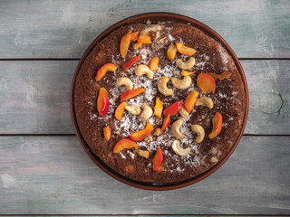 Apple pie with apple slices and cashew nuts on a brown plate top view on a brown background