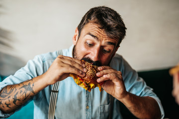 Handsome middle age man sitting in restaurant and enjoying in delicious burger.