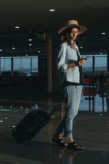 Tourist woman with hat and hand luggage waiting for the flight at the airport.