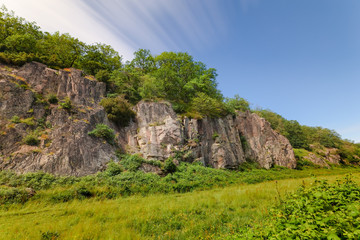 Felswand mit Grün vor blauem Himmel mit ziehenden Wolken