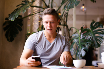 Young confident businessman working with documents and smartphoneat cafe.
