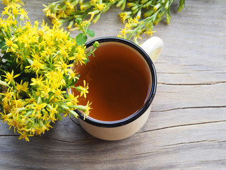 Medical herb Hypericum with yellow flowers and herbal tea in an enameled mug on a wooden stand, top view. Useful plant Hypericum perforatumfor use in alternative medicine