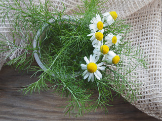 Medical chamomile flower bouquet with a napkin on a wooden background, top view, copy space. Useful herb matricaria chamomilla for use in alternative medicine and cosmetology