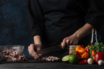 Chef cuts seafood, octopus for cooking, on the background of vegetables, oriental cuisine, asian food.Thai cuisine, cookery and recipe book