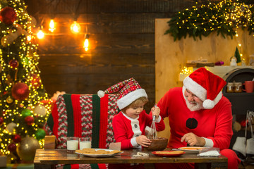 Kid Santa Claus enjoying in served gingerbread cake and milk. Santa Father and son having fun near Christmas tree and celebrate christmas at home. Funny kid make Christmas cookies.