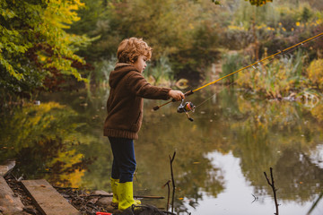 Kid with fishing-rod. Child fishing at autumn lake.