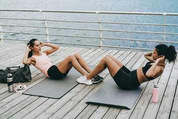 Image of focused multinational sportswomen working out on mats