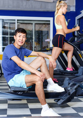 Fototapeta na wymiar Portrait of satisfied athletic smiling positive male resting during workout in fitness club