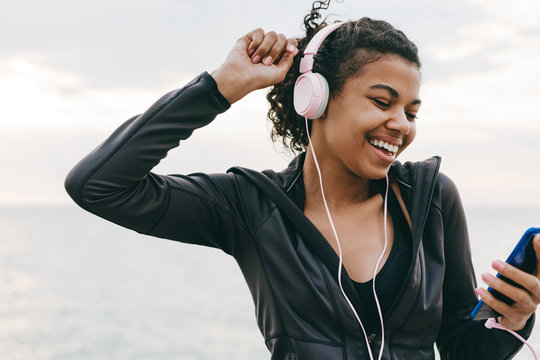 Image of smiling african american woman using cellphone and headphones