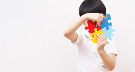 Portrait of young cute Asian kid hold and put together colorful puzzles pieces, and cover his face. World autism awareness day, Mental health care and Child development concept