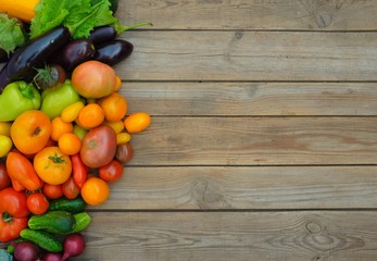 Many different colorful vegetables lie on a wooden board on the left side. There is free space for writing advertising text.. Harvest and summer season concept.