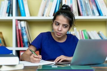 Young indian female student learning with books and computer