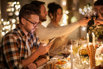 holidays and people concept - man with smartphone at dinner party with friends at home