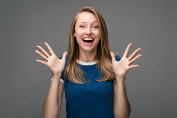 Fototapeta na wymiar Positive Young female with blonde straight hair smiling and spreads her hands to the side. Human emotions concept