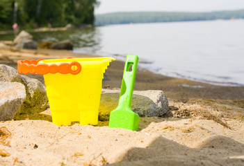 children's toys stand on the sand on the beach, a yellow bucket and a shovel for playing in the sand. activity on the beach