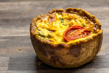 Little gourmet tomato and egg custard tartlet isolated on brown kitchen work top - savoury small quiche background