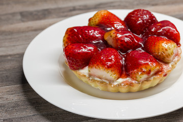 Small strawberry tart with cheesecake filling and shortcrust pastry base on white porcelain plate - delicious mini cheese cake