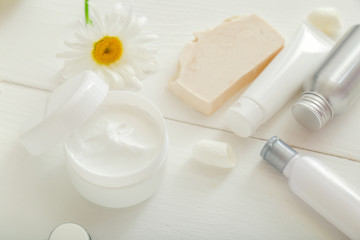 Moisturizer skin cream in white jar with chamomile flowers set white skincare products soap in tubes and bottles. Mockup white plastic jar for moisturizer skin cream, lotion on white background.