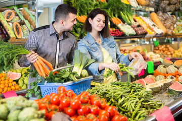 Young positive couple choosing fresh vegetables in grocery shop
