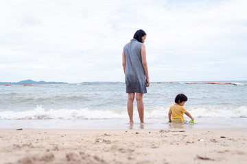 Mother and 3 years old asian kid playing on the beach. Background for family vacation and recreation.