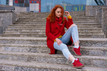 girl sitting on the steps in a red jacket and jeans