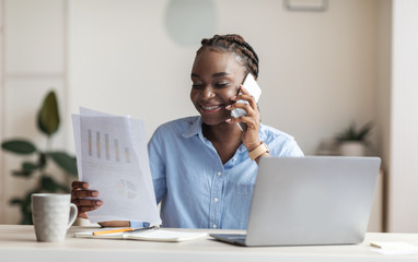 Successful black businesswoman checking financial reports and talking on cellphone in office